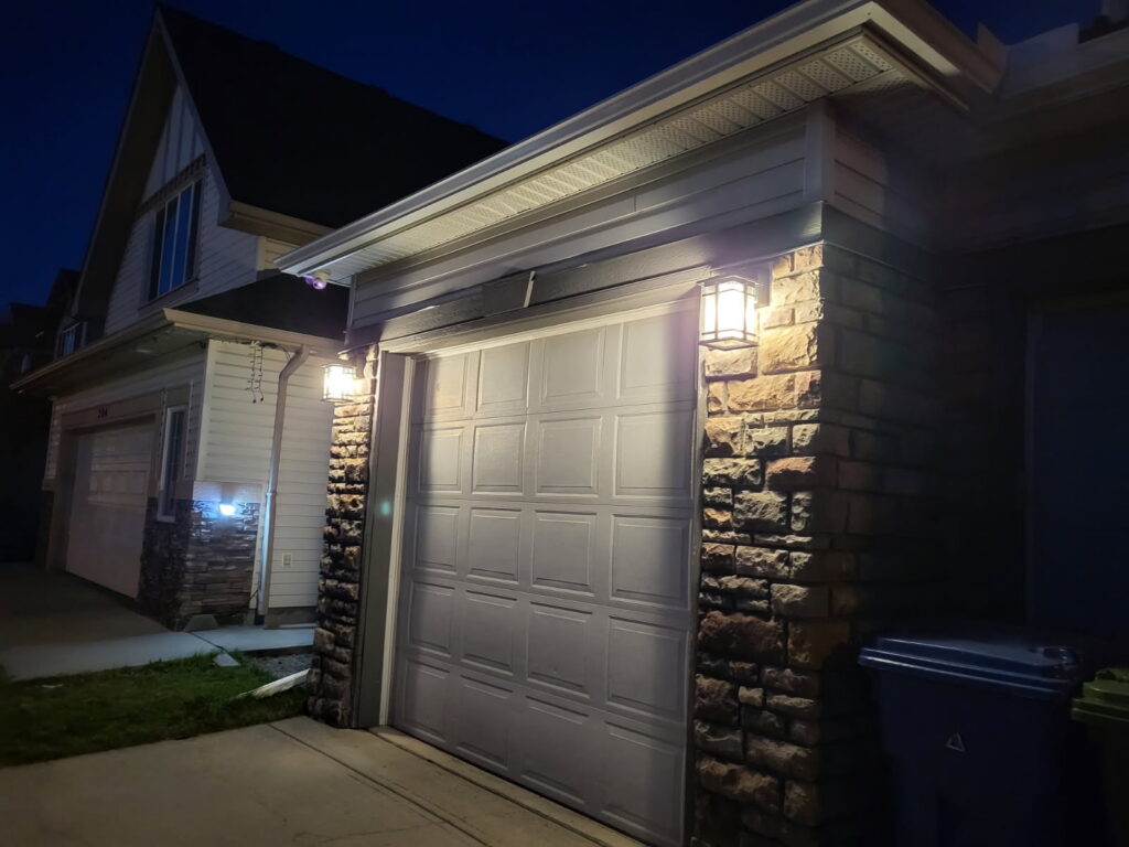 Two new lantern lights glowing on stone pillars of a Chestermere home's garage at night