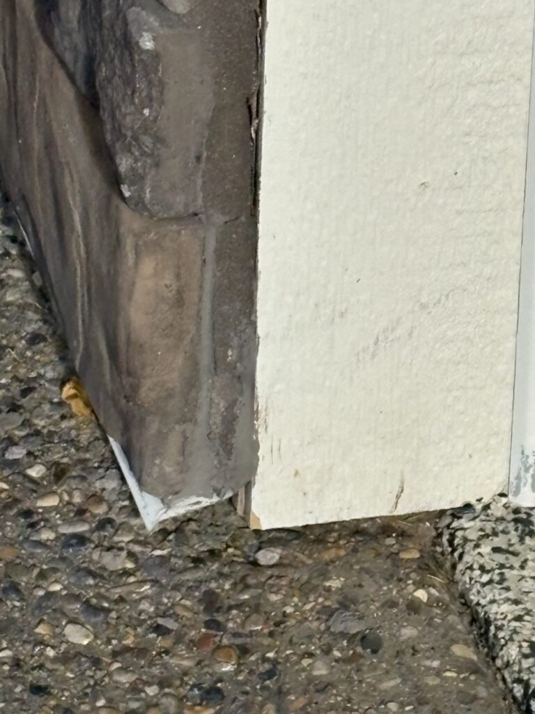 Exterior stone veneer wall corner beside a painted wall by Calgary Repairs