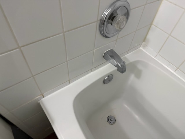 White bathtub with chrome faucet and shower controls against white tiled bathroom wall, showing completed plumbing fixture work by Calgary Repairs.